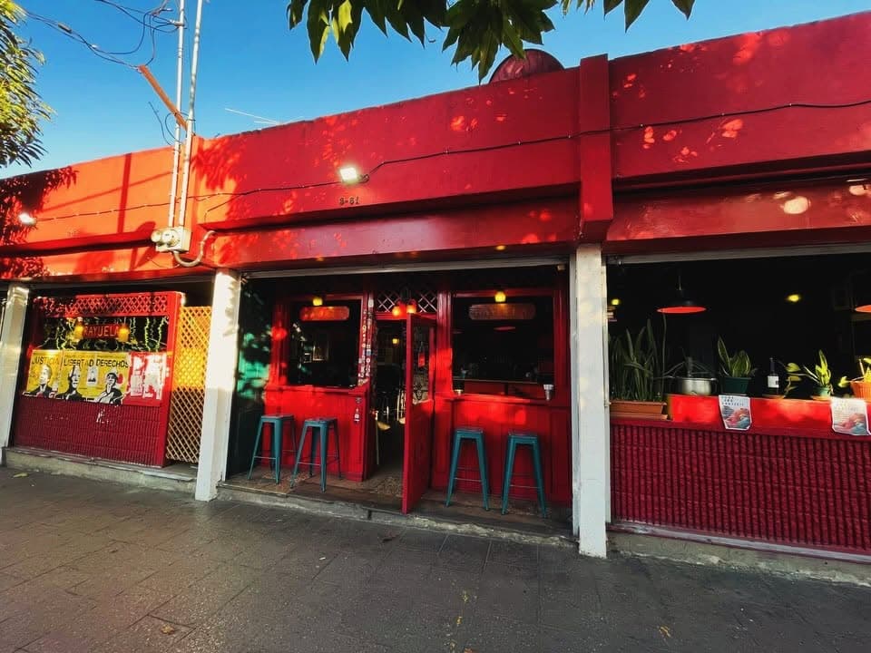 Fachada roja de Rayuela con bancos turquesa
